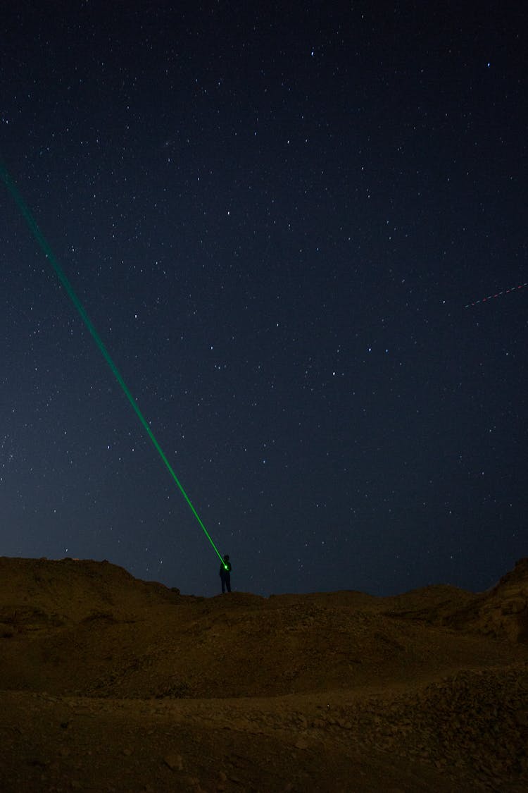 A Person Using A Green Laser Flash Light At Night