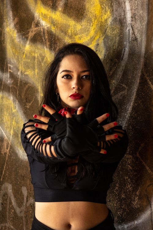 Free Portrait of a woman in a black crop top posing with gloves against a grungy backdrop, exuding confidence and style. Stock Photo