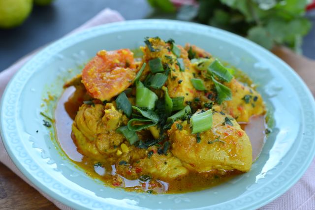 A close-up of spicy chicken dish garnished with green onions and herbs, served on a plate.