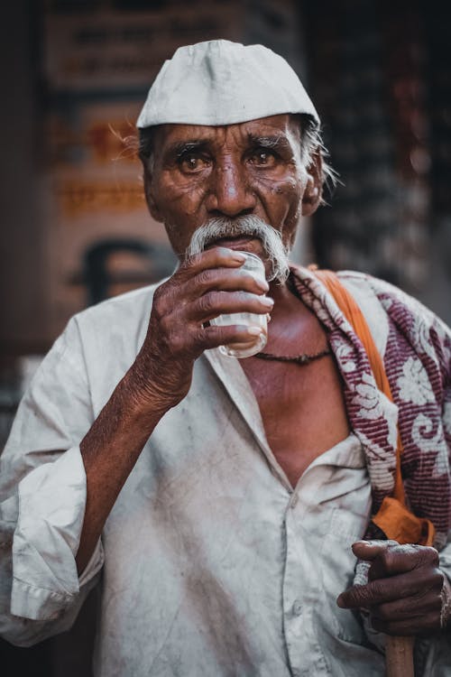 An Elderly Man Holding a Glass while Wearing a Cap