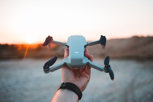 Close-up of a hand holding a drone against a scenic sunset backdrop outdoors.