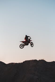 Motorcycle rider performing a high jump against a clear sky, showcasing thrilling stunt mastery.