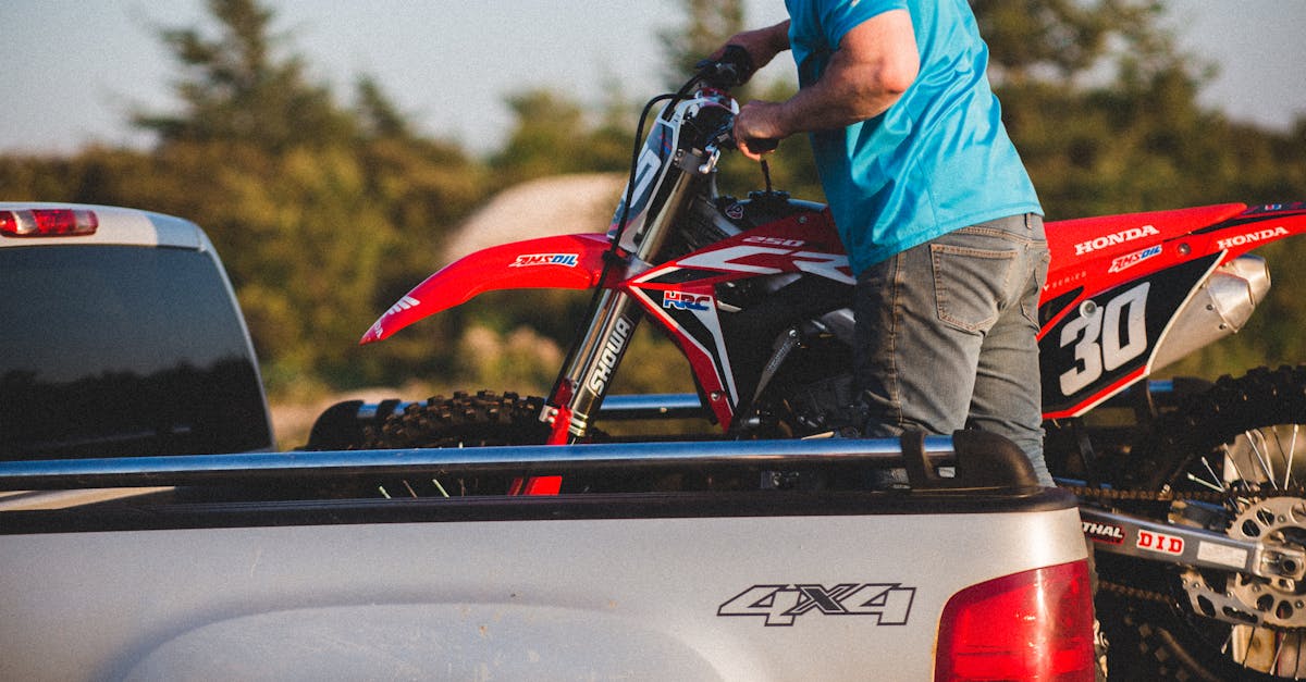 A man in blue loads a Honda motorcycle into a pickup truck at sunset, outdoors.