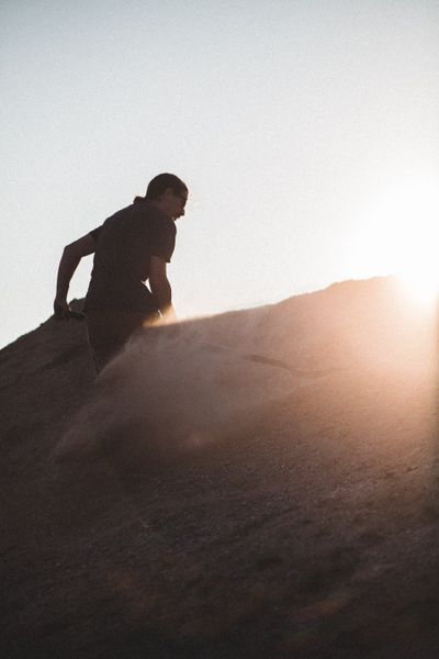 Silhouette climbing a sand ridge at sunset, photo by Erik Mclean on Pexels