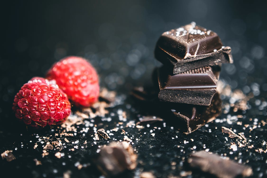 Free Close-Up Photo Of Stacked Chocolates Bars Beside Raspberries Stock Photo