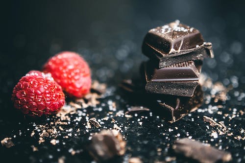 Free Close-Up Photo Of Stacked Chocolates Bars Beside Raspberries Stock Photo