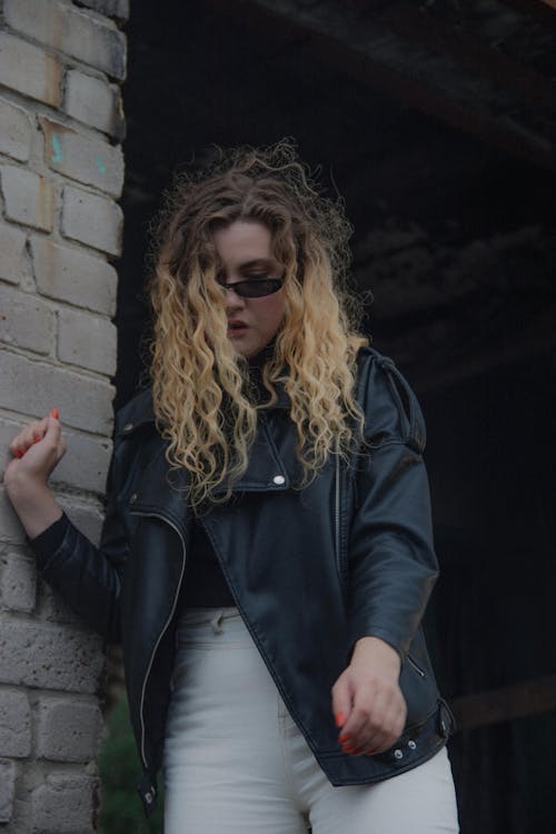Woman in Black Leather Jacket Standing Beside Brick Wall