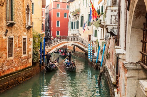 People Riding on Boat on River Between Concrete Buildings