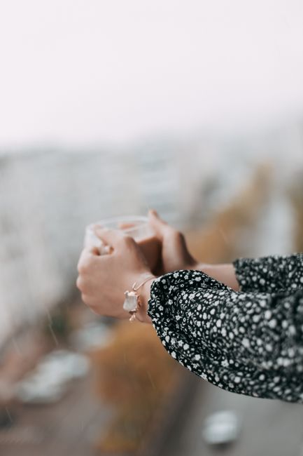 A person holds a hot drink with a blurred cityscape view, evoking a cozy atmosphere.