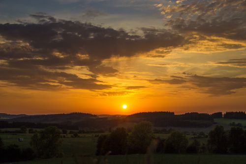 Free Dramatic sunset over rolling hills and fields with a warm, vibrant sky. Stock Photo