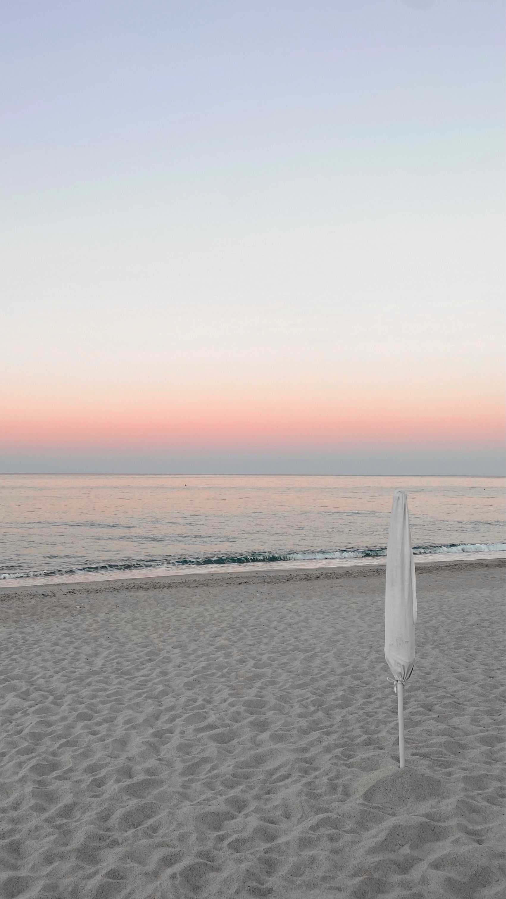 Empty pastel beach at sunset with a single closed umbrella — photo by Karina Nesterchuk on Pexels