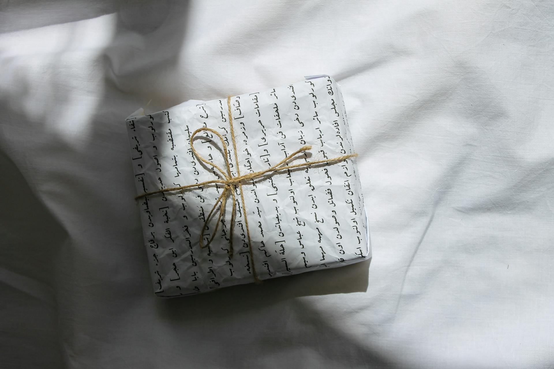 A beautifully wrapped gift on a white surface, tied with twine string and script-patterned paper.