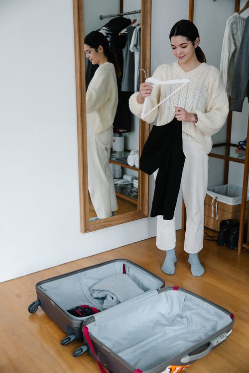 Free Young woman packing clothes, reflecting in mirror indoors. Stock Photo