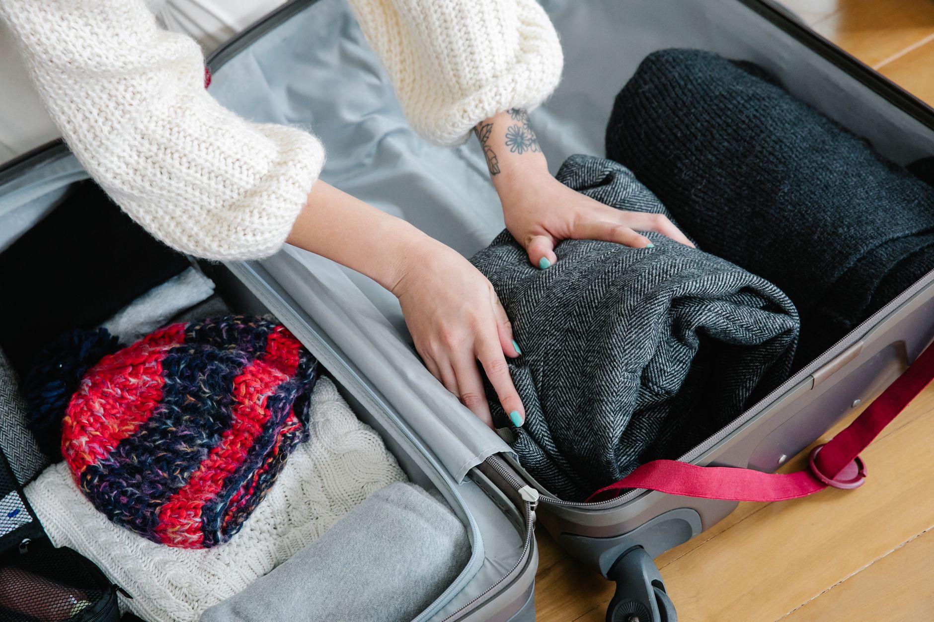 Close-up of hands packing cozy sweaters and knitwear into a suitcase for a trip.