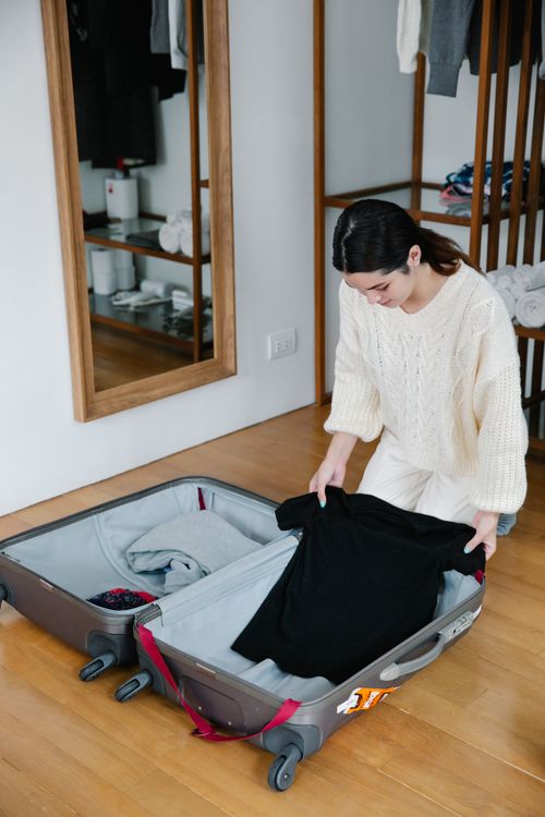 Free Woman kneeling on wooden floor packing clothes into luggage for travel preparation. Stock Photo