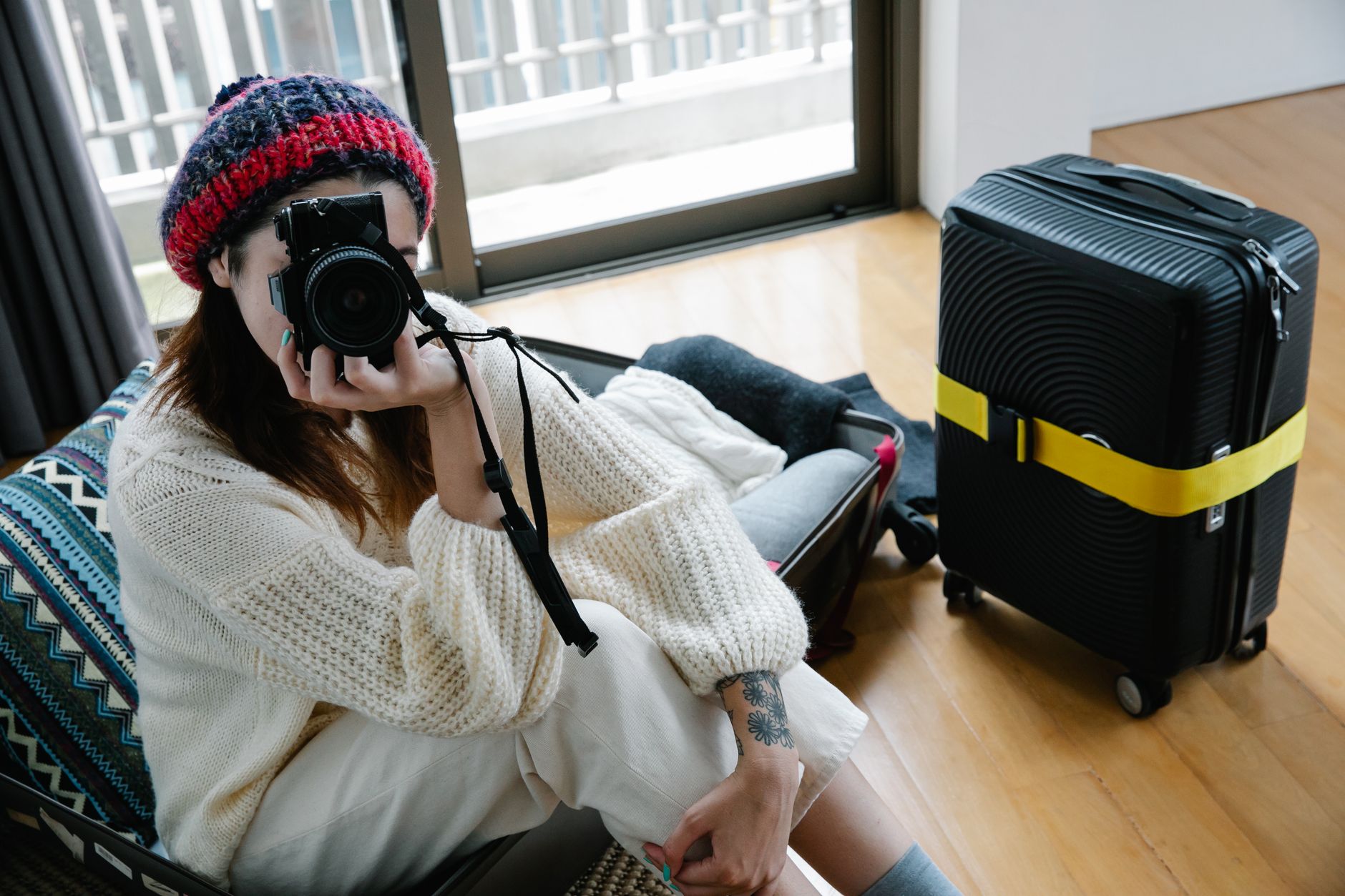 A young woman with a camera and suitcase sitting inside a modern room.
