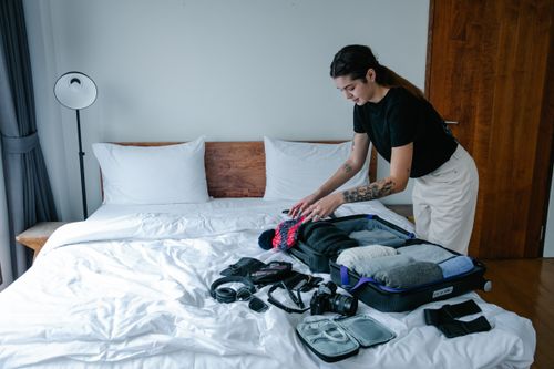 Free Young woman organizing luggage on a bed in a stylish indoor setting, preparing for travel. Stock Photo
