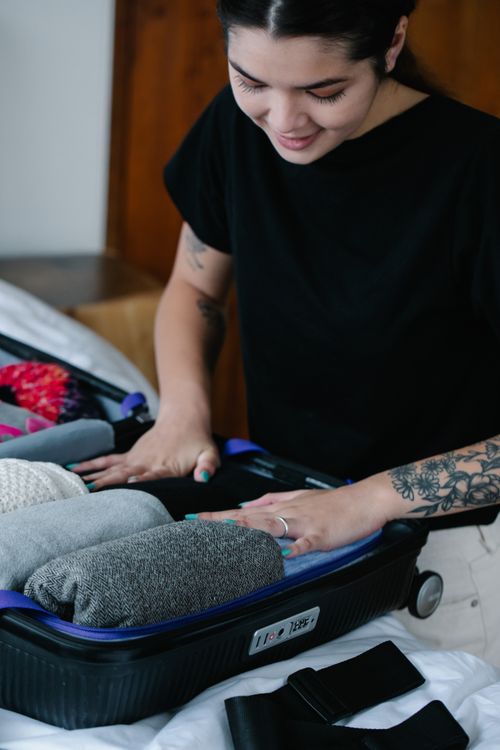 Free Woman with tattoos packs clothes into a suitcase in a cozy room. Stock Photo