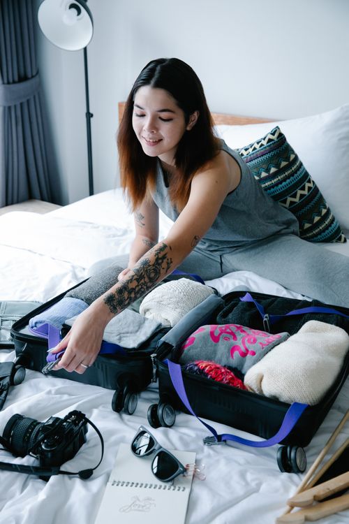 Free Woman with tattoos packing a suitcase in a modern bedroom setting. Stock Photo