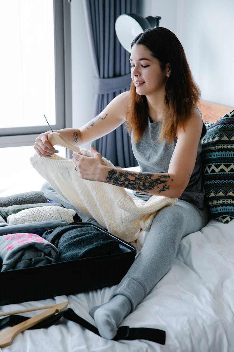 Woman Sitting On The Bed While Packing Clothes