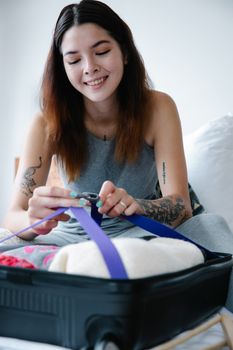 Tattooed woman packing suitcase with clothes while smiling indoors.