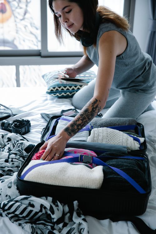 Free Woman with tattoo packs suitcase indoors during day, preparing for travel. Stock Photo