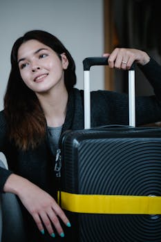 Smiling young woman holding modern suitcase in relaxed indoor setting.