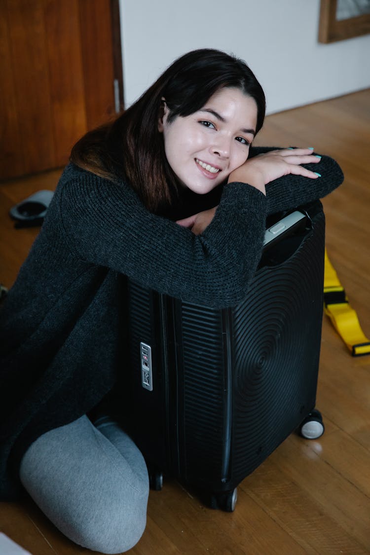 Woman In Black Sweater Sitting On Floor Hugging The Luggage 