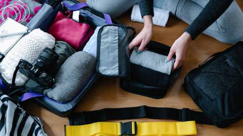 A woman arranging clothes and accessories into a suitcase, preparing for travel.