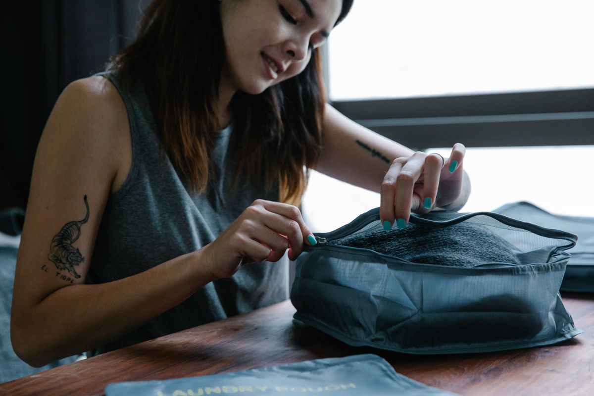 A grey fabric cube getting zipped shut on a table, stuffed fuller than the manufacturer probably intended. This is the load-in, not the photo shoot.