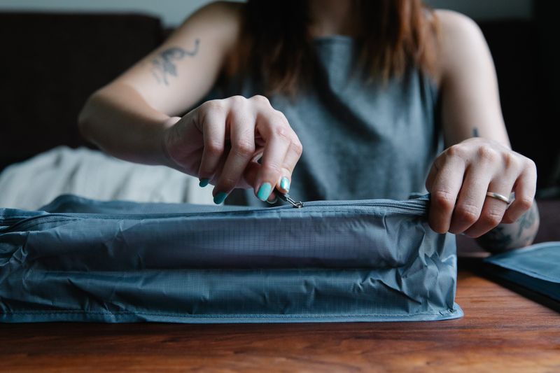 Close-up of a woman with manicured nails zipping a travel bag indoors.