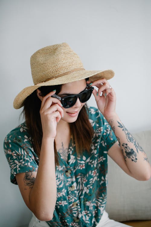 Free A Pretty Woman in Floral Top and with a Sun Hat Wearing Sunglasses Stock Photo