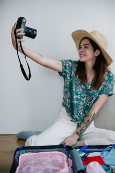 A woman captures a travel selfie while packing her suitcase indoors, ready for adventure.