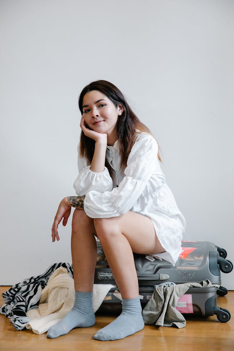 Woman Wearing White Long Sleeve Sitting On A Luggage