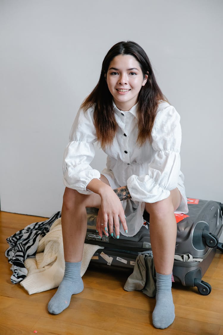 A Woman In White Dress Sitting On A Luggage