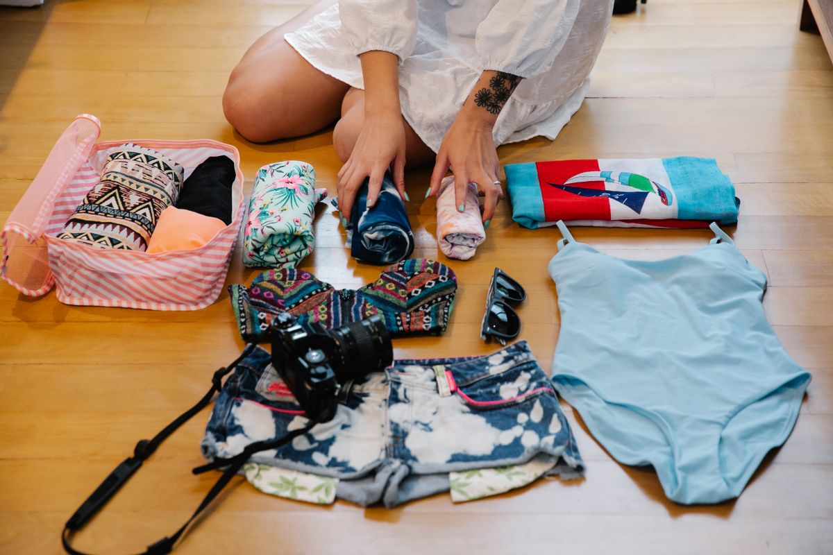 Everything laid out on a wood floor before load-in: shirts, a camera, sunglasses, one pink cube waiting its turn, nothing zipped yet.