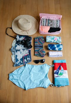 Flat lay of summer travel essentials including clothing, camera, and accessories on wooden floor.