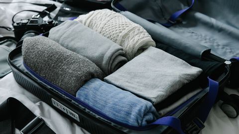 Open suitcase filled with neatly folded clothes on bed, ready for travel preparation.