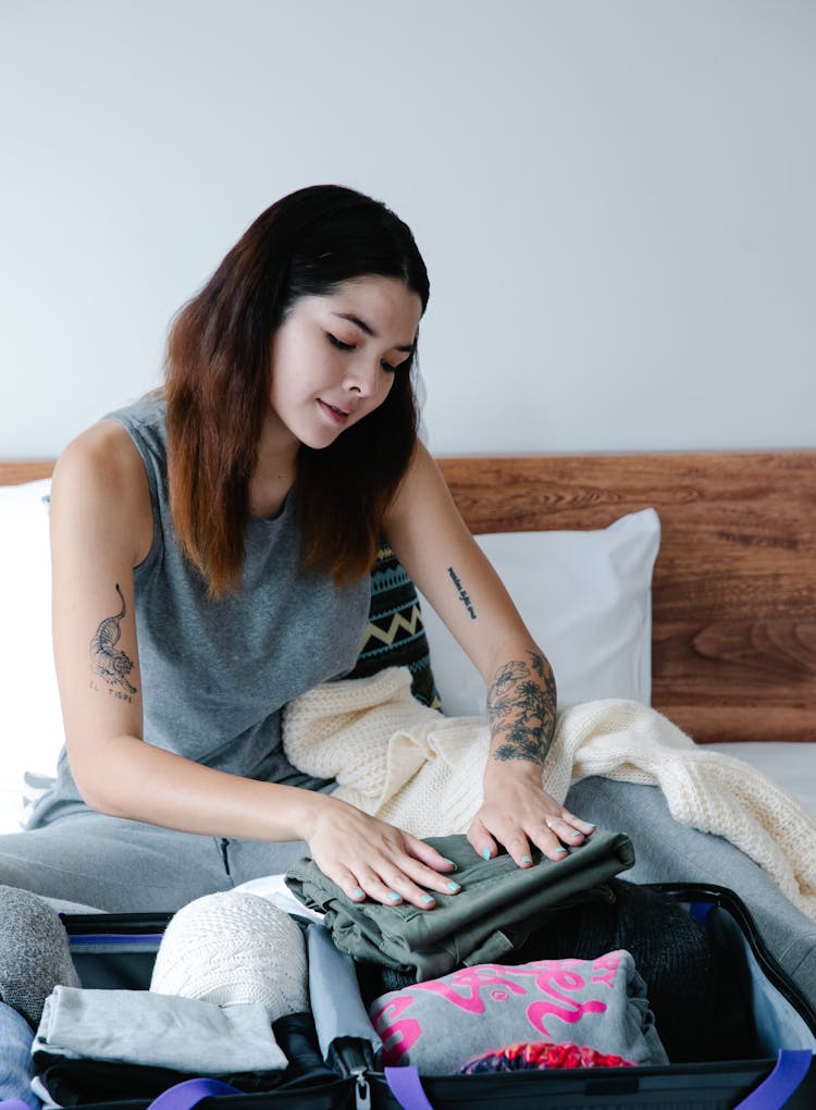 A Woman In Gray Tank Top Folding Clothes On A Suitcase