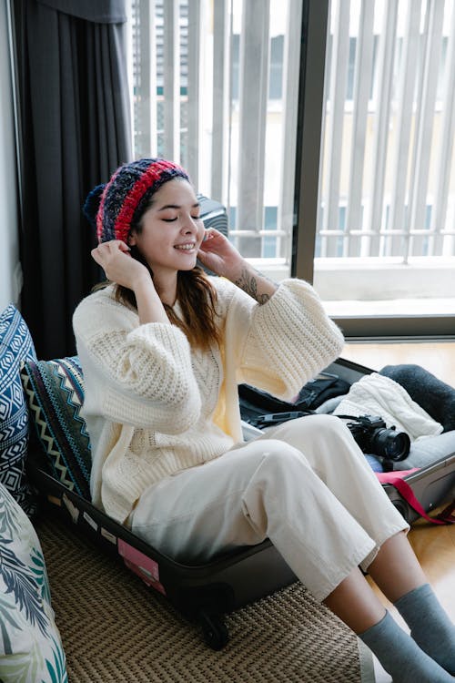 A Woman in White Sweater Sitting on Her Luggage