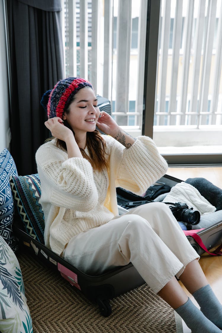 A Woman In White Sweater Sitting On Her Luggage