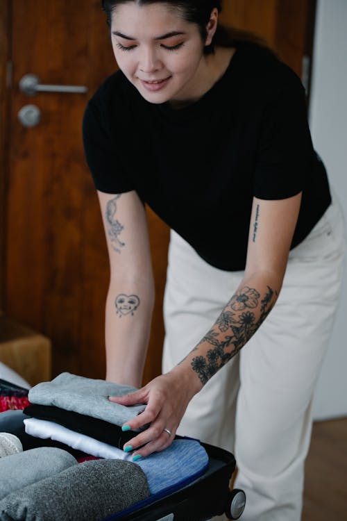 A Woman in Black Crew Neck T-shirt Holding a Stack of Folded Clothes