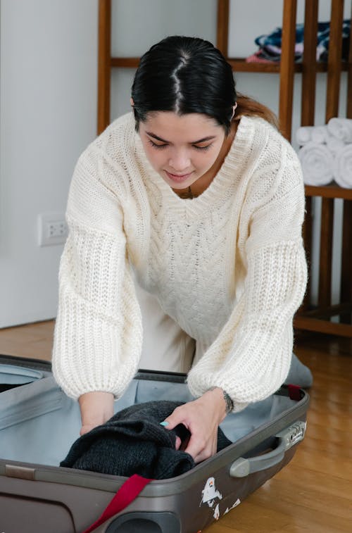 Free A Woman in White Sweater Packing Clothes in a Luggage Stock Photo