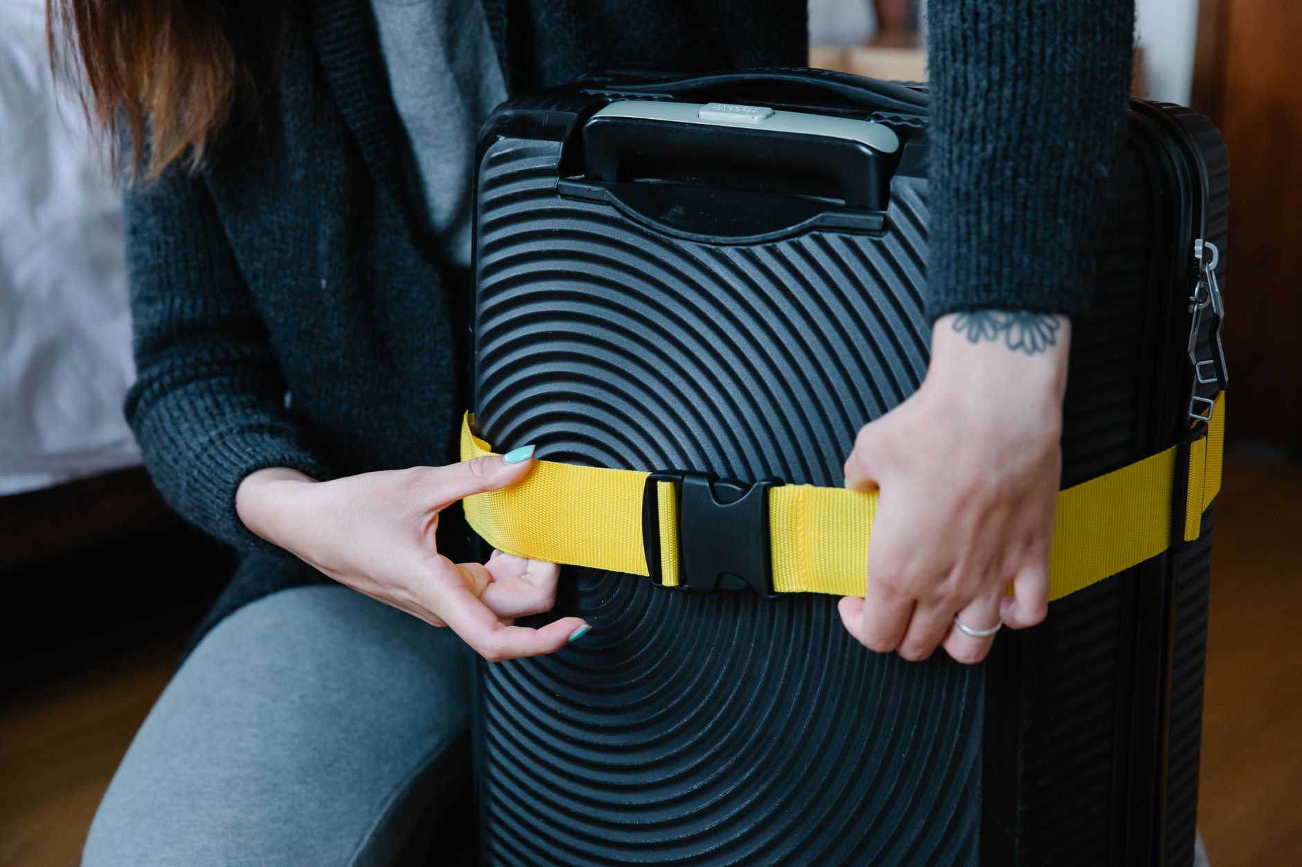 Close-up of hands fastening a bright yellow strap around a black suitcase.