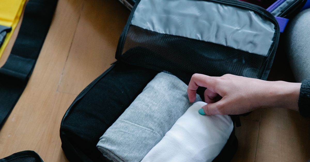 Organizando a mala maternidade Mãos dobrando roupas dentro de um organizador de mala