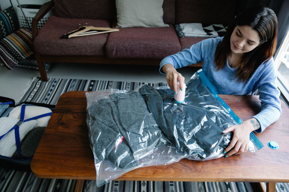 Woman using vacuum cleaner to compress home storage bag on table