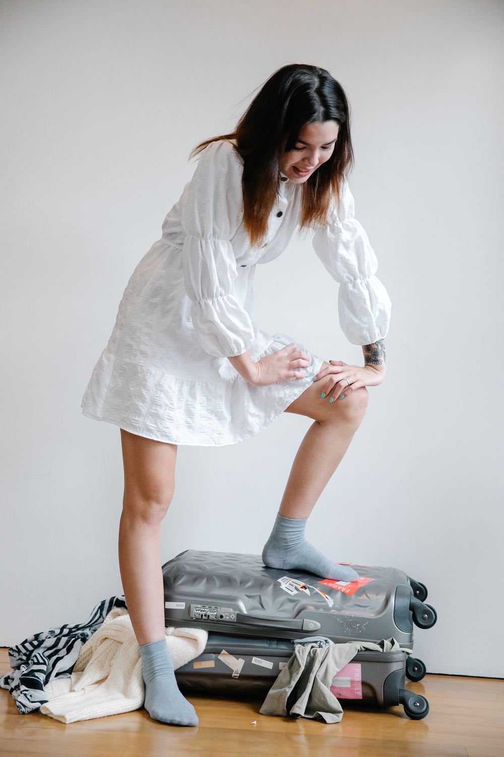 Woman in a light travel dress standing beside a suitcase indoors before a trip