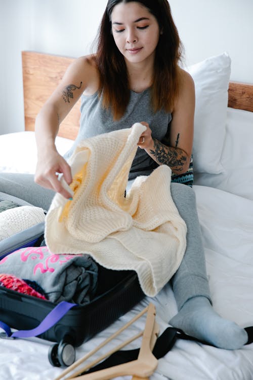 Free Woman Sitting on Bed While Folding a Sweater Stock Photo