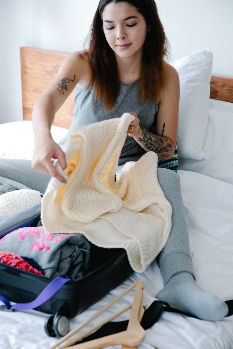 Woman Sitting On Bed While Folding A Sweater