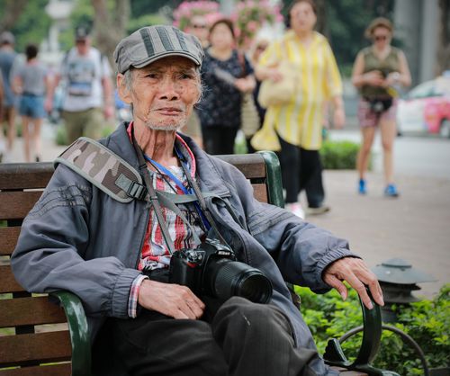 Free Senior man with camera sitting on a park bench capturing life's moments. Stock Photo